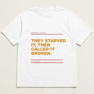 Front of a white tee reading "They starved it, then called it broken." with the Housing Justice page address printed under it